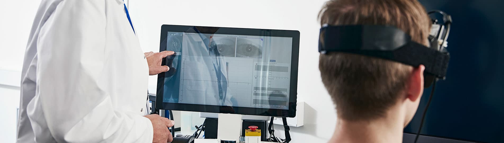 Clinician operating VisualEyes software on touch screen while patient wearing VNG goggles is looking toward a flat screen TV