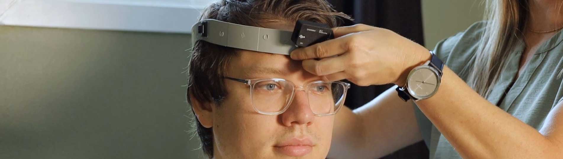 Clinician attaching VORTEQ™ head sensor to a headband fixated on a young man's head