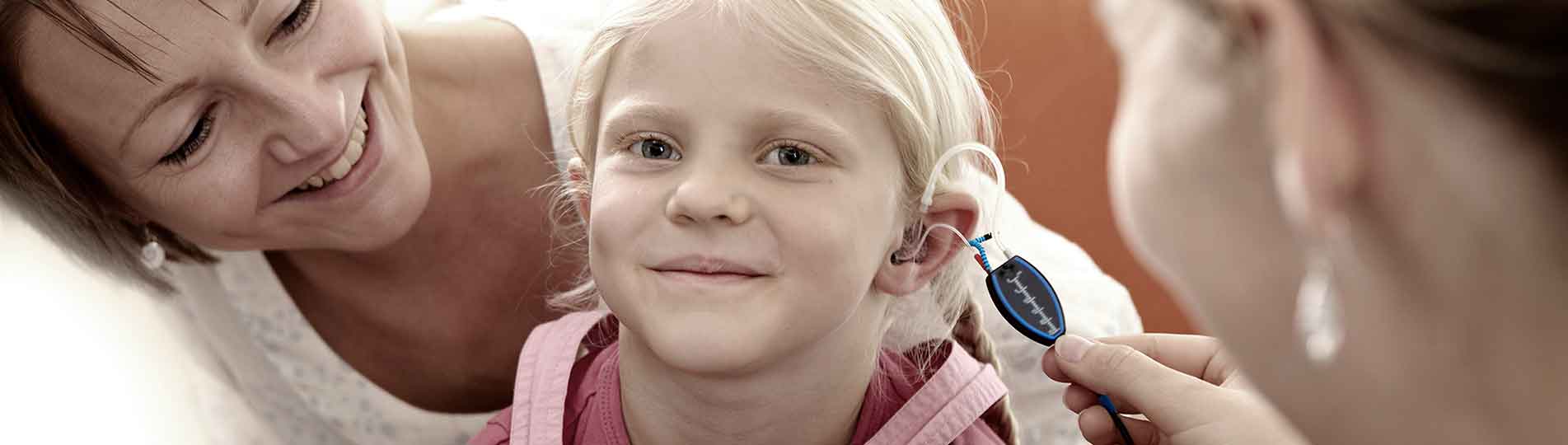 Female clinician performing real-ear measurement in young girl that is sat on her mother's lap