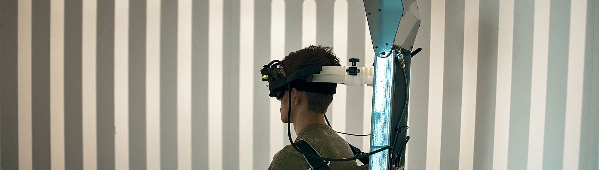 Patient strapped into the enclosed Orion Comprehensive chair and wearing VNG goggles. The light from the optokinetic drum above the patient is displaying a visual pattern across the wall of the booth enclosure.