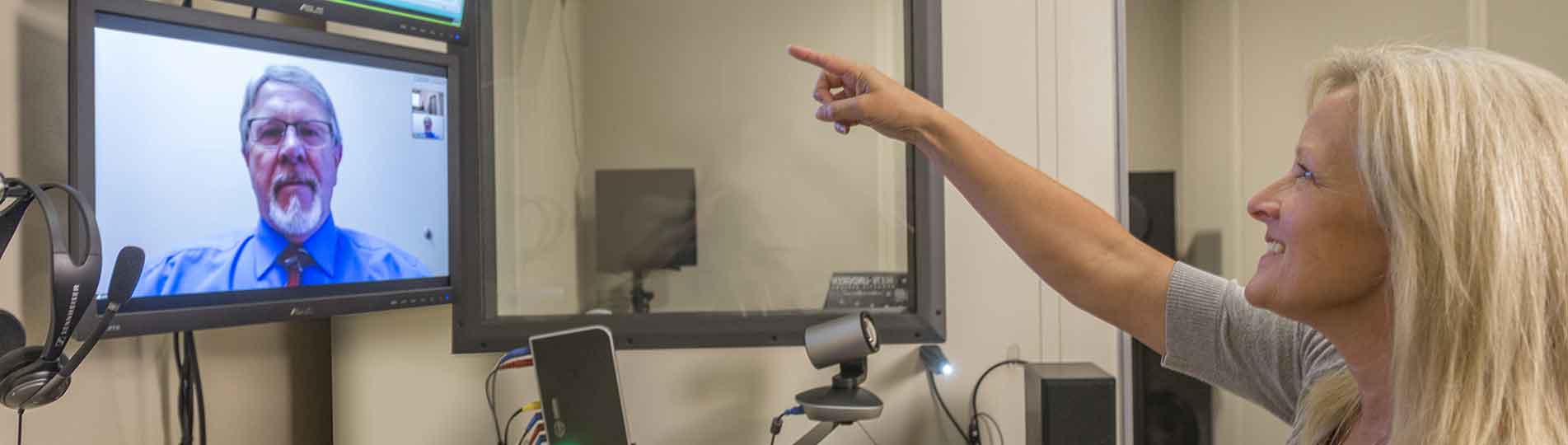 Female patient pointing toward audiometry software with male clinician looking on remotely via web cam