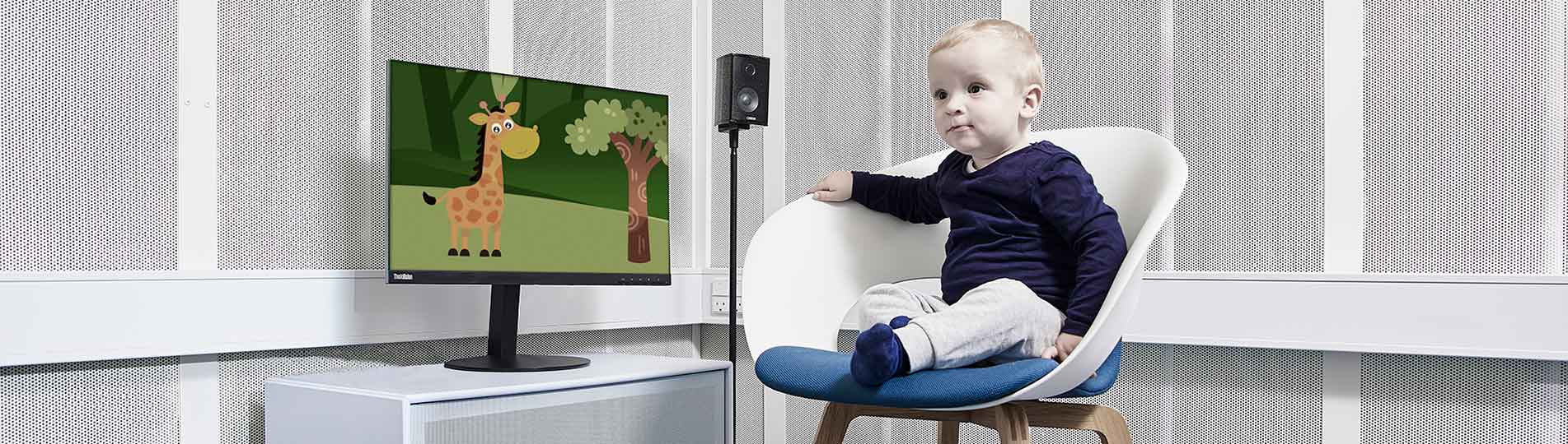 Little boy sat in a white chair next to a computer screen showing an animated giraffe